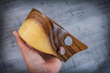 Load image into Gallery viewer, Hand holding a handcrafted acacia Kuksa mug with ergonomic double handle, close-up of natural wood grain against a textured grey background.