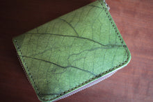 Laden des Bilds im Galerie-Viewer, Nahaufnahme eines grünen Portemonnaies aus recycelten Blättern auf dunklem Holz. Die einzigartige Blattaderung und die präzisen Nähte sind deutlich sichtbar.
Close-up of a green wallet made from recycled leaves on dark wood. The unique leaf veining and precise stitching are clearly visible.