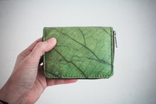 Laden des Bilds im Galerie-Viewer, Nachhaltiges, veganes Portemonnaie aus grünem Blattmaterial mit Reißverschluss, seitlich in einer Hand vor weißem Hintergrund gehalten – umweltfreundliche Geldbörse für Damen und Herren.
Sustainable vegan wallet made from green leaf material with zipper, held sideways in a hand against a white background – eco-friendly unisex purse.