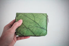 Laden des Bilds im Galerie-Viewer, A green wallet with a leaf pattern, held in a hand. The wallet has a zip closure and a textured surface, resembling a leaf's veins. The wallet is approximately 12 cm wide and 9 cm tall.
Nachhaltiges, veganes Portemonnaie aus grünem Blattmaterial mit Reißverschluss, seitlich in einer Hand vor weißem Hintergrund gehalten – umweltfreundliche Geldbörse für Damen und Herren.
Sustainable vegan wallet made from green leaf material with zipper, held sideways in a hand – eco-friendly unisex purse.