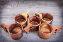 Laden des Bilds im Galerie-Viewer, Handcrafted Kuksa mugs made from acacia wood in Scandinavian design, five natural wooden cups with ergonomic handles, artfully arranged on a wooden table.
