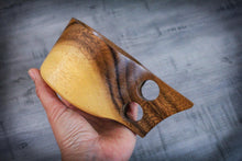 Laden des Bilds im Galerie-Viewer, Hand holding a handcrafted acacia Kuksa mug with ergonomic double handle, close-up of natural wood grain against a textured grey background.
