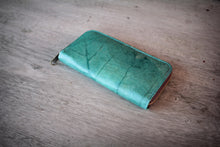 Laden des Bilds im Galerie-Viewer, Close-up of a sustainable, vegan turquoise wallet made from recycled leaves, focusing on the golden zipper and the visible leaf texture and stitching.
Nahaufnahme einer nachhaltigen, veganen Geldbörse in Türkis, hergestellt aus recycelten Blättern. Der goldene Reißverschluss und die sichtbare Blattstruktur sind im Fokus.
