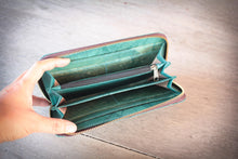 Laden des Bilds im Galerie-Viewer, Eine Hand präsentiert die geöffnete, handgefertigte Geldbörse in Türkis, hergestellt aus recycelten Blättern. Die Innenfächer und das zentrale Reißverschlussfach sind sichtbar.

A hand presenting the open, handmade turquoise wallet, made from recycled leaves. The interior compartments and central zippered pocket are clearly visible.
