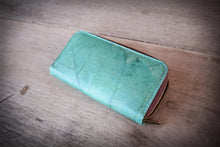 Laden des Bilds im Galerie-Viewer, Vegane Brieftasche in Türkis mit Reißverschluss, handgefertigt aus recycelten Blättern, liegt auf einem rustikalen Holztisch. Die einzigartige Blattstruktur bedeckt die gesamte Oberfläche.

Vegan turquoise zippered wallet, handcrafted from recycled leaves, resting on a rustic wooden table. The unique leaf vein structure covers the entire surface.
