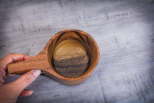 Laden des Bilds im Galerie-Viewer, Top-down view of a handcrafted Kuksa cup made from acacia wood, held in hand, showing natural wood grain and ergonomic handle
