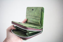 Laden des Bilds im Galerie-Viewer, Das geöffnete grüne Blattleder-Portemonnaie wird von einer Hand präsentiert, wobei das untere Reißverschlussfach für Münzen ebenfalls offensteht.
The open green leaf leather wallet presented by a hand, showing the card slots above and the open zippered coin compartment at the bottom.
