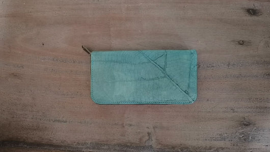 Dieses kurze Video zeigt die äußere Textur der türkisfarbenen Geldbörse aus recycelten Blättern und präsentiert anschließend die geräumige Innenaufteilung mit Reißverschlussfach und Kartenfächern. Perfekt für den täglichen Gebrauch und nachhaltig.

This short video demonstrates the exterior texture and 360° view of the turquoise recycled leaf leather wallet. It then shows the spacious interior layout, highlighting the zippered coin pocket and multiple card slots. Sustainable and practical for daily use.